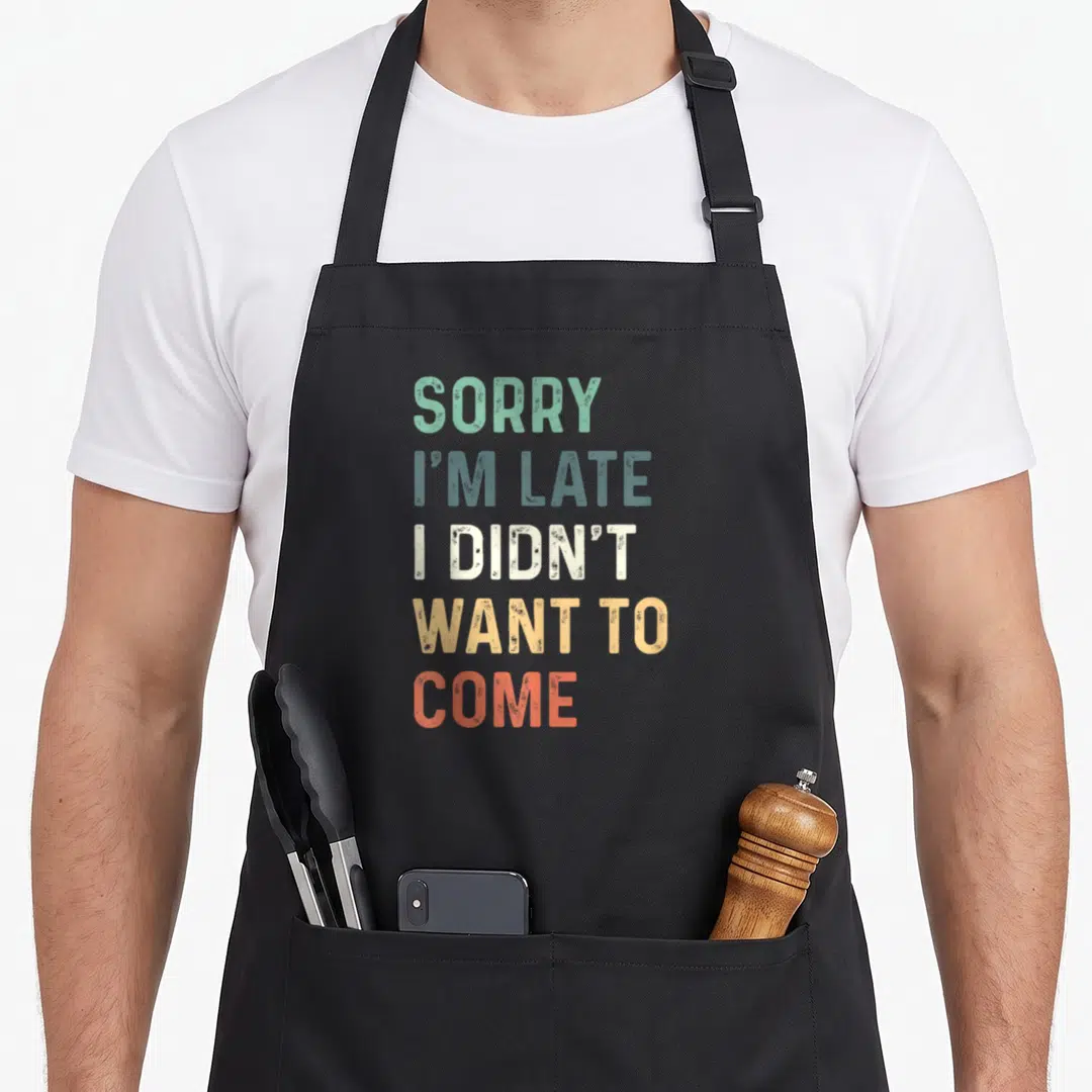 Didnt sorry im apron - Stacked SORRY I'M LATE text in green, blue-grey, white, yellow, and red-orange colors — shown on a black cotton canvas apron against a white background
