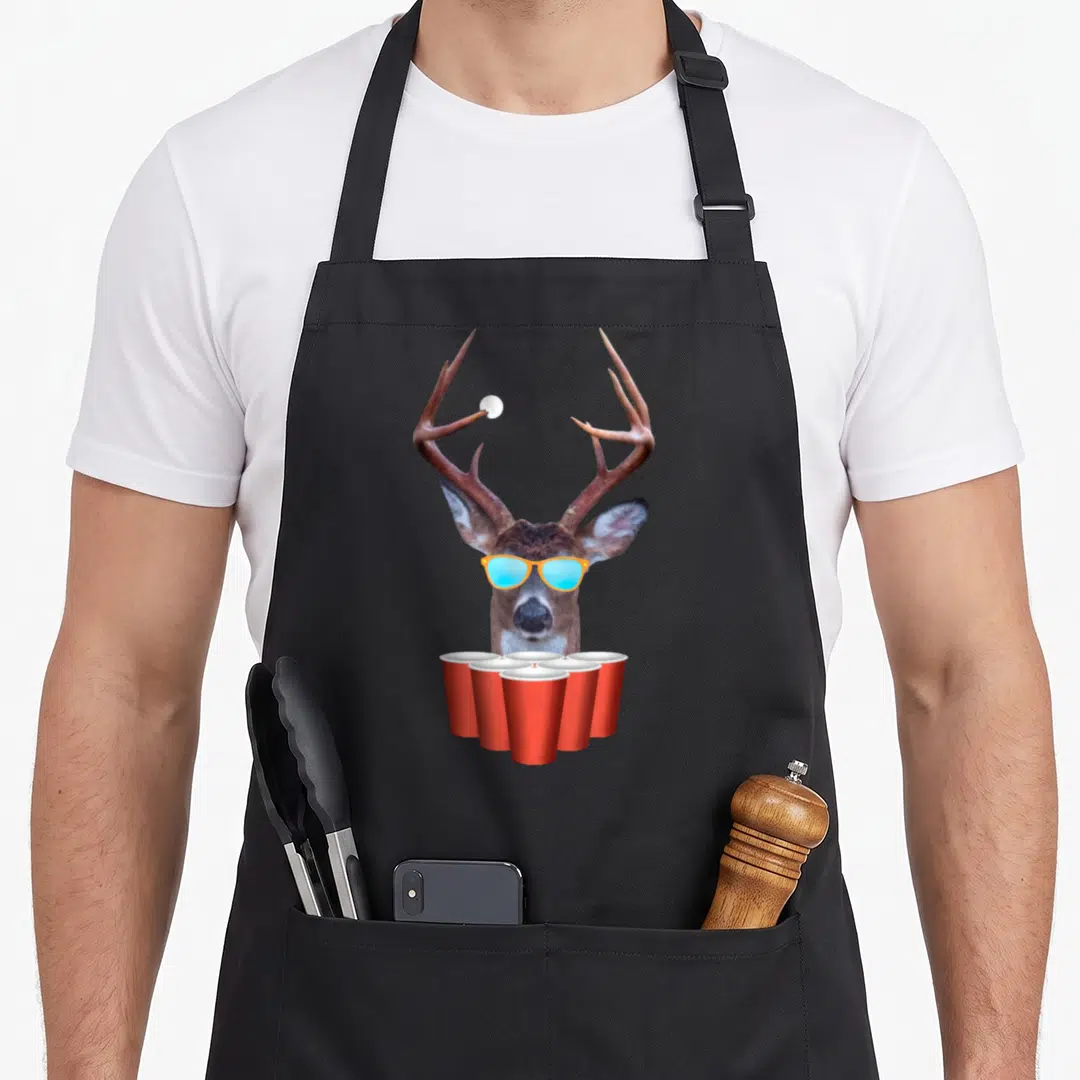 Deer beer pong apron - Photographic deer head with orange sunglasses, blue lenses, white ball on antler, five red cups — shown on a black cotton canvas apron against a white background