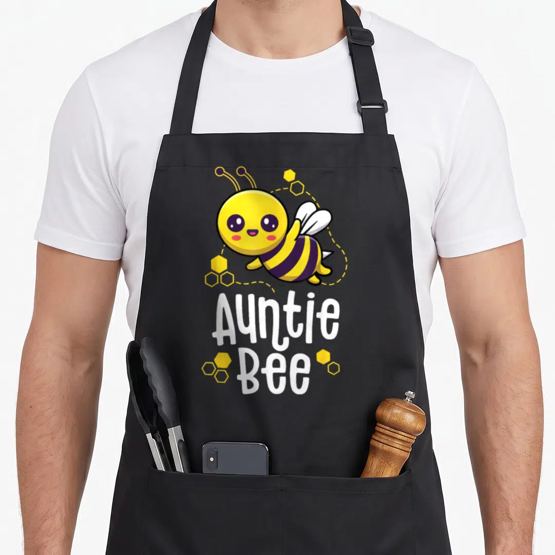 Family bee apron - Cartoon bee with yellow honeycomb cells and white Auntie Bee text — shown on a black cotton canvas apron against a white background