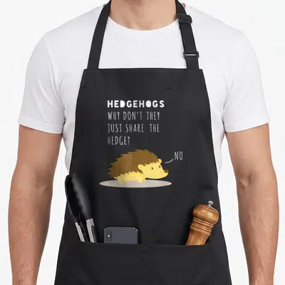 Wont funny hedgehog apron - Cartoon hedgehog facing right saying NO to sharing a hedge pun — shown on a black cotton canvas apron against a white background