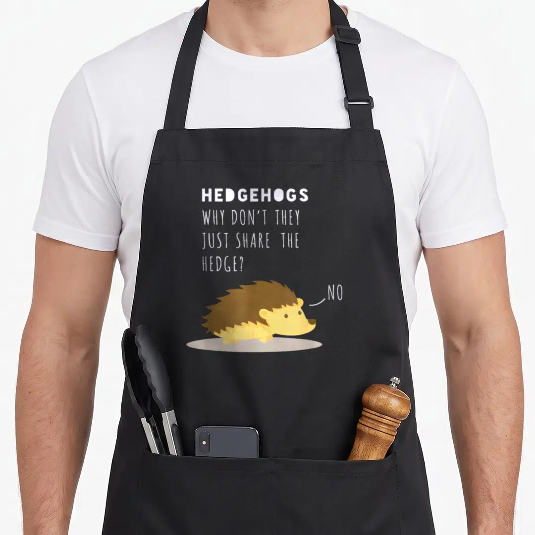 Wont funny hedgehog apron - Cartoon hedgehog facing right saying NO to sharing a hedge pun — shown on a black cotton canvas apron against a white background