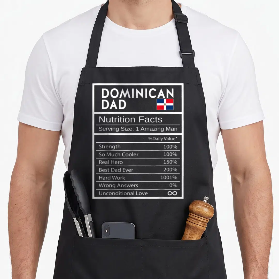 Dominican nutrition pride apron - Nutrition facts label graphic with Dominican flag and stats like 1001% Hard Work — shown on a black cotton canvas apron against a white background