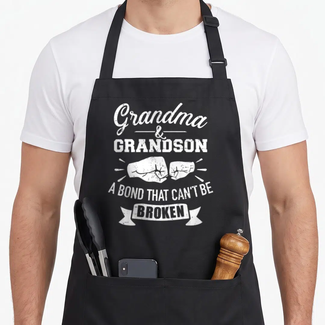 Bond grandma apron - White distressed text Grandma Grandson with two fists bumping and broken ribbon banner — shown on a black cotton canvas apron against a white background