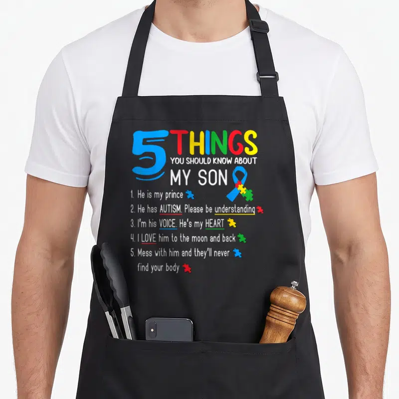 Autistic dad and son aprons - Colorful text listing 5 things about an autistic son with a blue ribbon and puzzle pieces — shown on a black cotton canvas apron against a white background