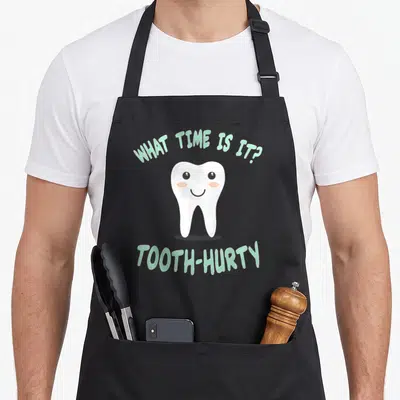 Joke dentist apron - Smiling cartoon tooth with mint green text WHAT TIME IS IT?, TOOTH-HURTY — shown on a black cotton canvas apron against a white background