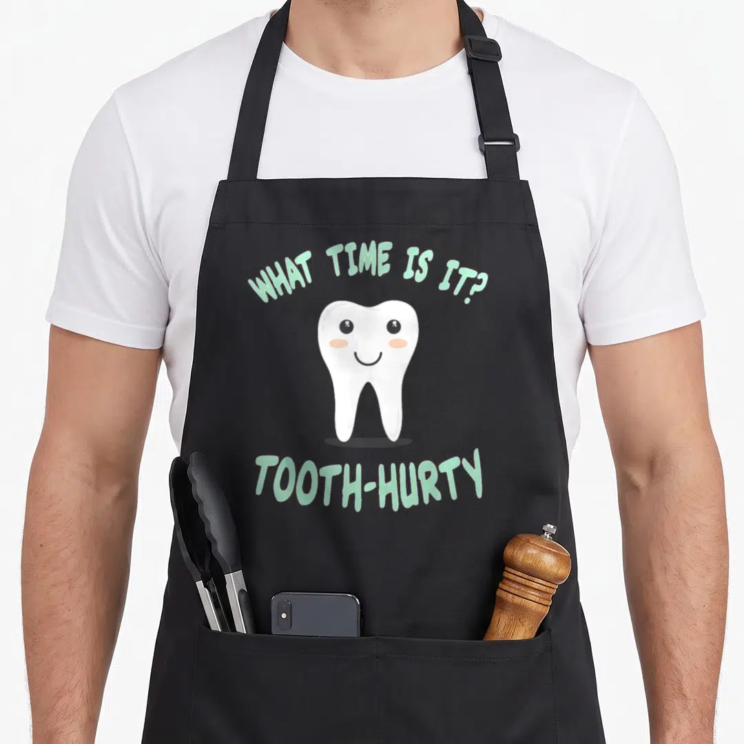 Joke dentist apron - Smiling cartoon tooth with mint green text WHAT TIME IS IT?, TOOTH-HURTY — shown on a black cotton canvas apron against a white background