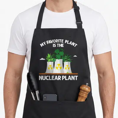 Nuclear engineering apron - My Favorite Plant Is The Nuclear Plant text with green plants growing from three grey — shown on a black cotton canvas apron against a white background