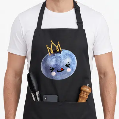Blueberry anime apron - Cartoon blueberry with crown, pink cheeks, and yellow crown details — shown on a black cotton canvas apron against a white background