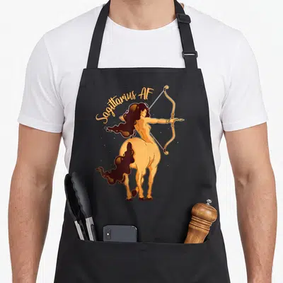 Sagittarius horoscope apron - Female centaur archer aiming bow with arched Sagittarius AF text in tan and brown — shown on a black cotton canvas apron against a white background