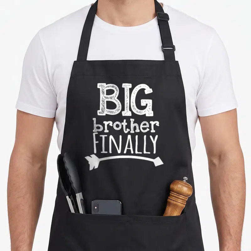Finally brother love apron - White stacked text BIG brother FINALLY with curved arrow pointing left — shown on a black cotton canvas apron against a white background