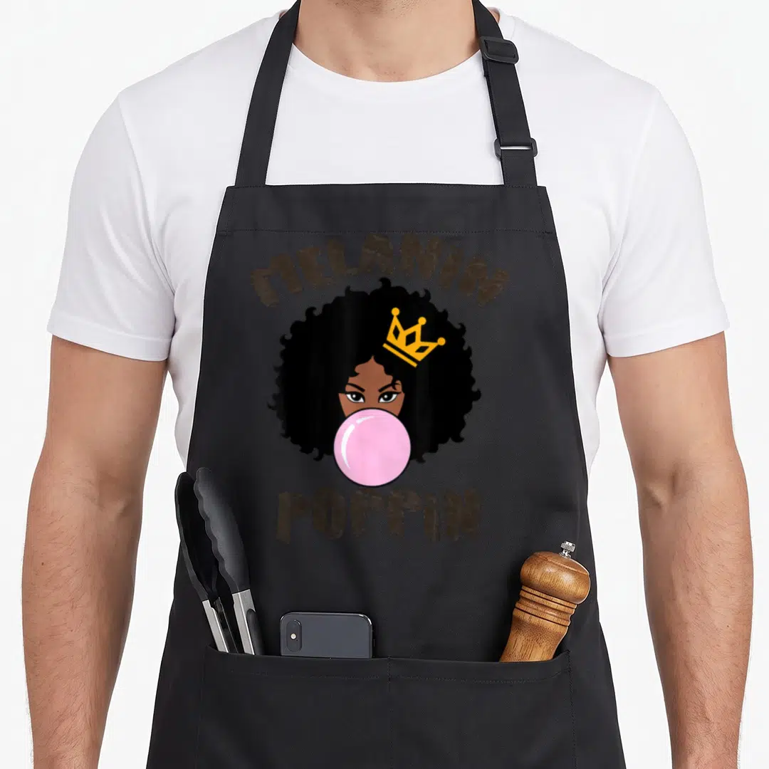 Melanin history apron - Cartoon woman with crown and pink bubblegum surrounded by brown text MELANIN POPPIN — shown on a black cotton canvas apron against a white background