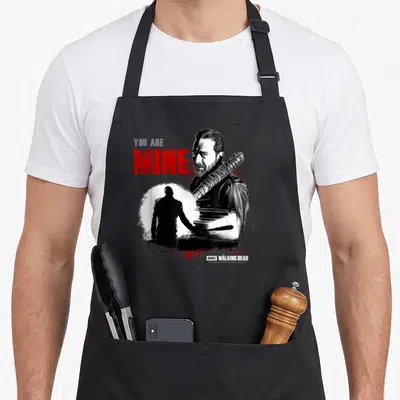 Negan walking apron - Distressed man portrait with barbed wire bat and YOU ARE MINE text in red and grey — shown on a black cotton canvas apron against a white background