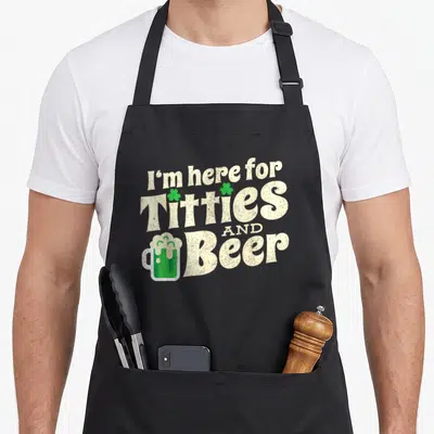 Titty beer apron - Stacked text I'm here for Titties AND Beer with two shamrocks and a green beer mug in distressed — shown on a black cotton canvas apron against a white background