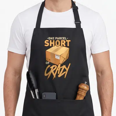 Parcel postal aprons - Cartoon cardboard box with text One Parcel Short of Crazy in tan and brown — shown on a black cotton canvas apron against a white background