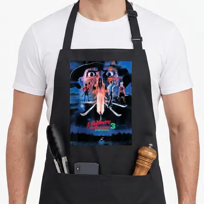 Nightmare warrior apron - Freddy Krueger face four figures on blades A Nightmare On Elm Street 3 Dream Warriors text — shown on a black cotton canvas apron against a white background
