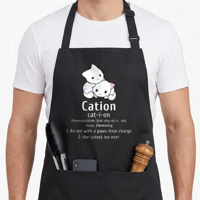 Pawsitive chemistry apron - Two stacked white cartoon cats above cation dictionary definition text with pink and blue — shown on a black cotton canvas apron against a white background