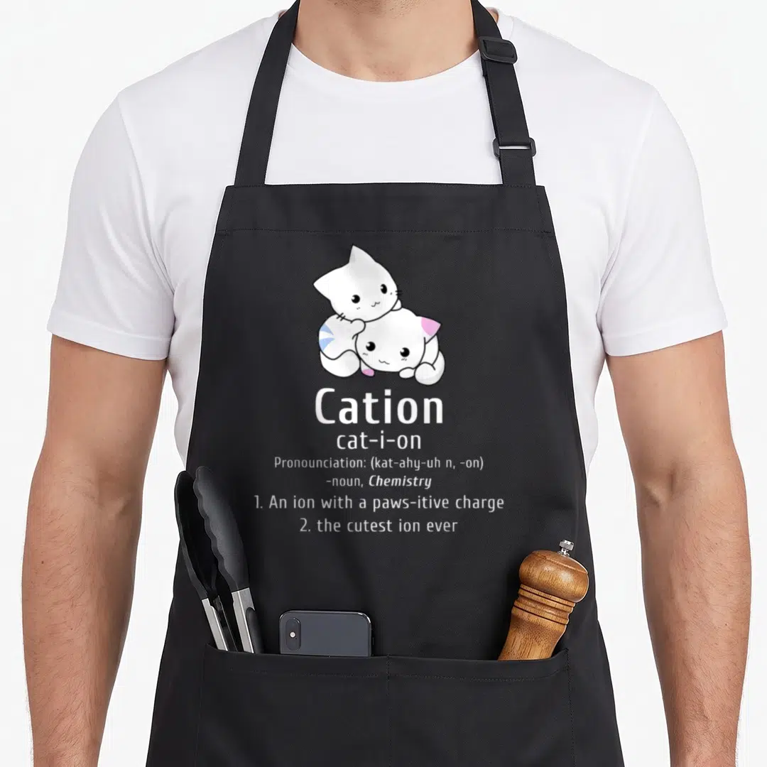 Pawsitive chemistry apron - Two stacked white cartoon cats above cation dictionary definition text with pink and blue — shown on a black cotton canvas apron against a white background