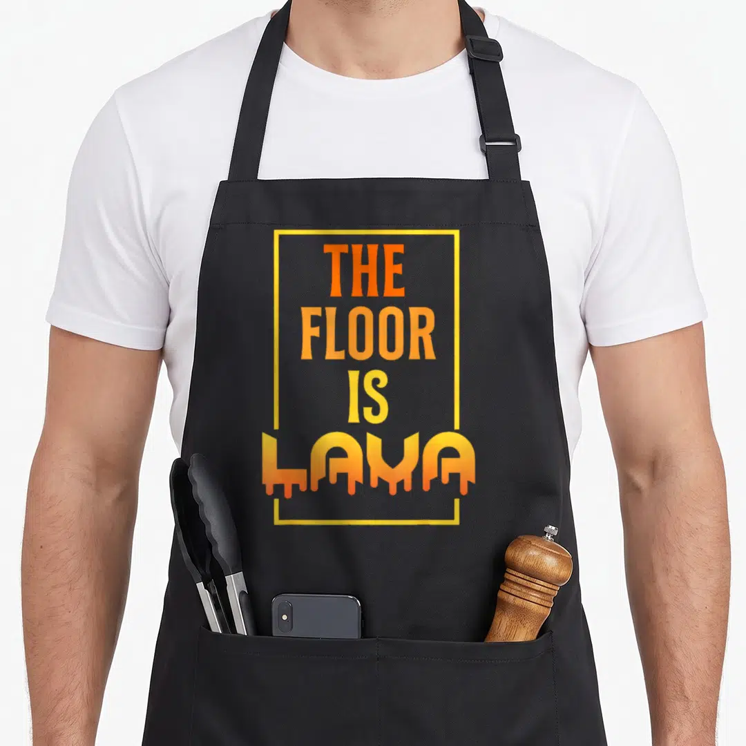 Floor parkour apron - Orange and yellow text reading THE FLOOR IS LAVA with drips inside a yellow rectangle — shown on a black cotton canvas apron against a white background