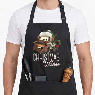 Car christmas apron - Brown cartoon truck wearing green hat with white trim and wreack on back above Christmas Wishes — shown on a black cotton canvas apron against a white background