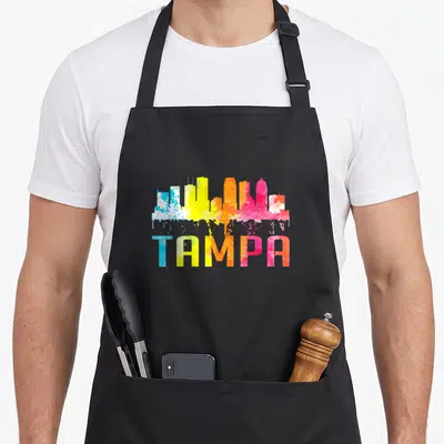 Watercolor florida apron - Colorful watercolor skyline silhouette with TAMPA text below — shown on a black cotton canvas apron against a white background