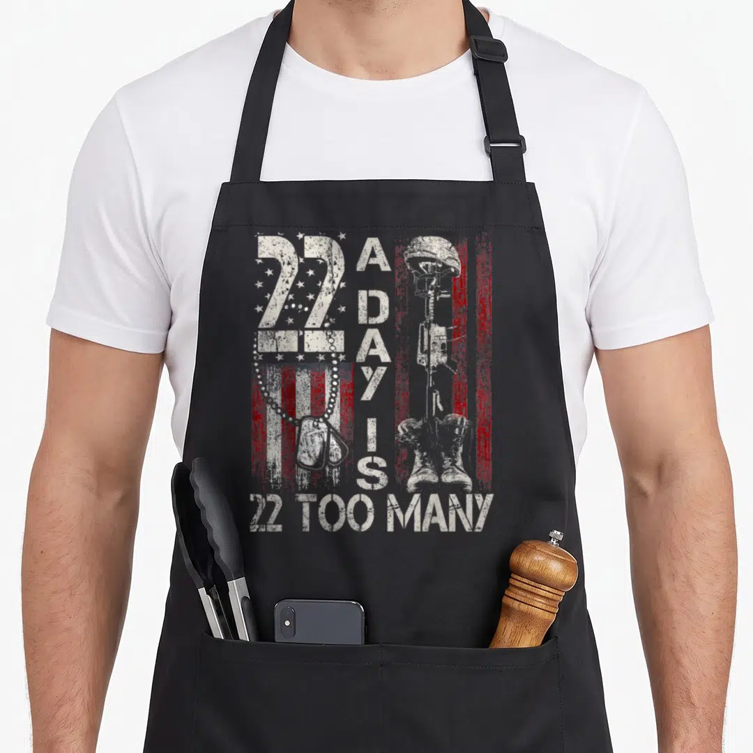 Many veterans day apron - 22 A Day Is 22 Too Many text with dog tags and fallen soldier memorial on distressed flag — shown on a black cotton canvas apron against a white background