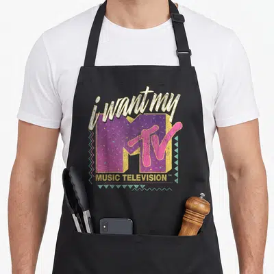 Mtv colorful aprons - Retro MTV logo with i want my text, purple M, pink TV, and mint zigzag borders — shown on a black cotton canvas apron against a white background