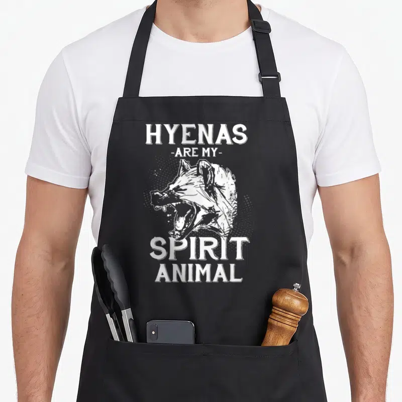 Africa animal apron - White hyena head illustration with halftone dots and distressed text reading HYENAS ARE MY SPIRIT — shown on a black cotton canvas apron against a white background