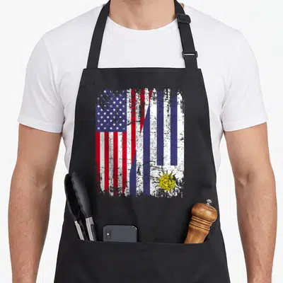 Uruguayan american flag apron - Distressed diagonal merge of USA and Uruguay flags in red white blue and yellow — shown on a black cotton canvas apron against a white background