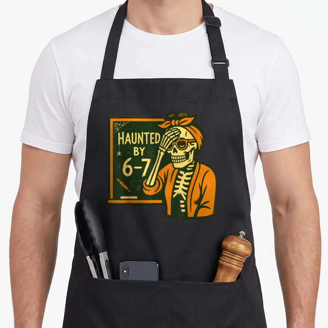 Haunted teacher apron - Skeleton covering eyes next to chalkboard reading Haunted By 6-7 in orange and green — shown on a black cotton canvas apron against a white background