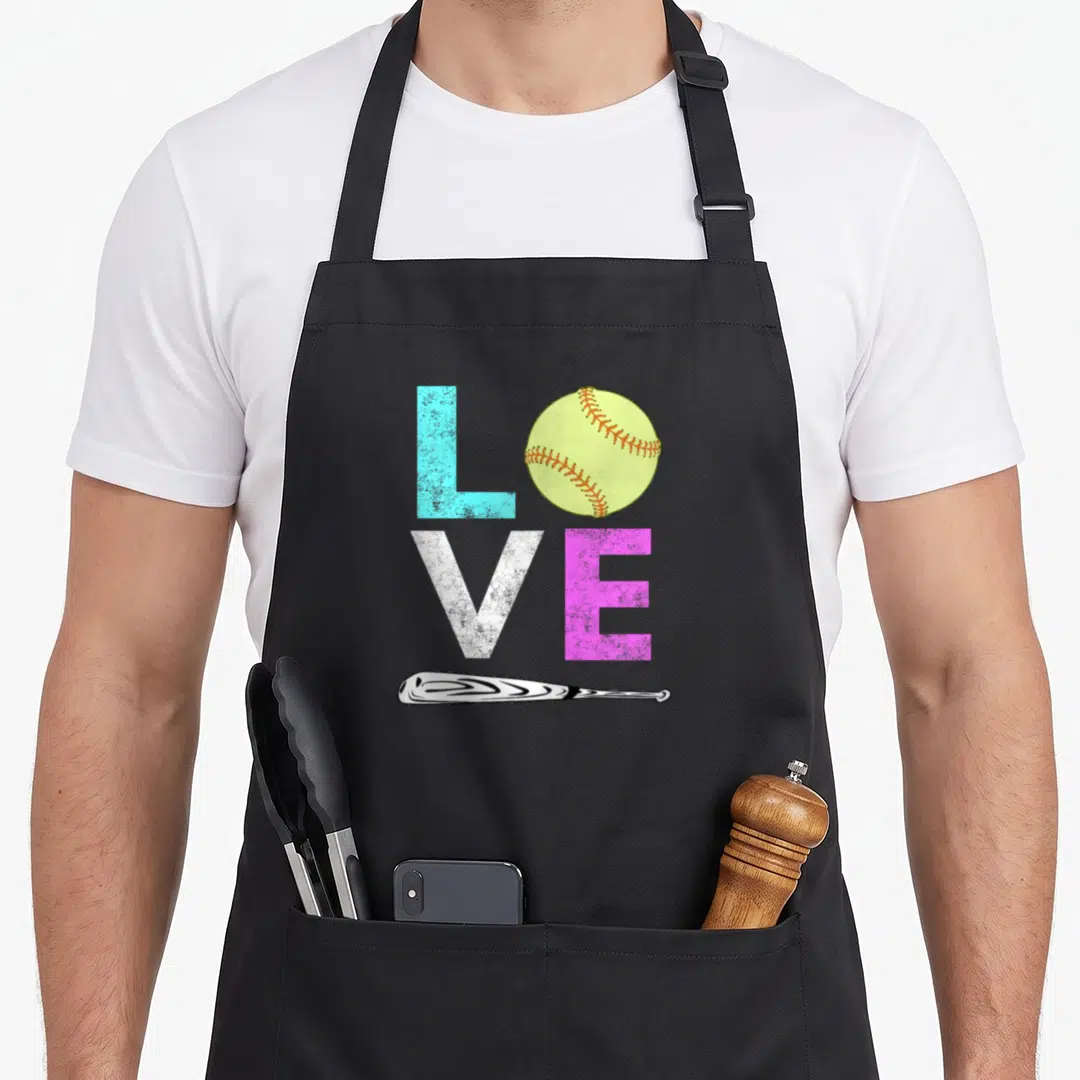 Softball birthday apron - LOVE spelled with blue L, yellow softball, white V, pink E, and horizontal bat — shown on a black cotton canvas apron against a white background