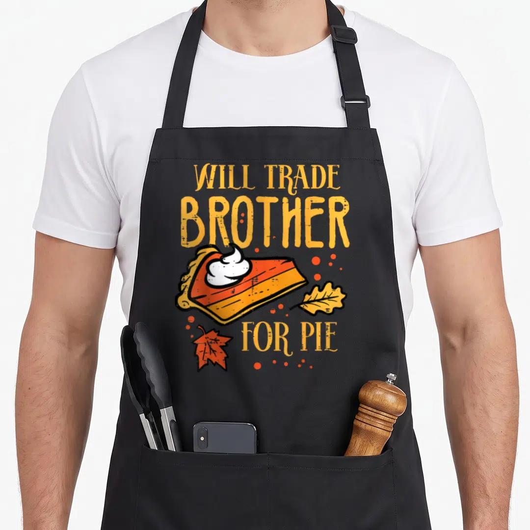 Trade thanksgiving apron - Will Trade Brother For Pie text with pie slice, cream, and autumn leaves — shown on a black cotton canvas apron against a white background
