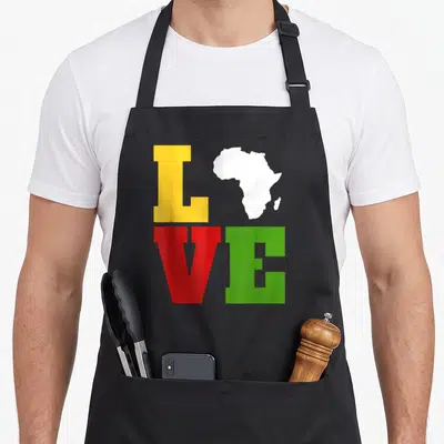 Afrocentric african apron - LOVE text grid with Africa map replacing O in yellow red green white — shown on a black cotton canvas apron against a white background