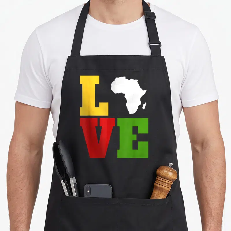 Afrocentric african apron - LOVE text grid with Africa map replacing O in yellow red green white — shown on a black cotton canvas apron against a white background