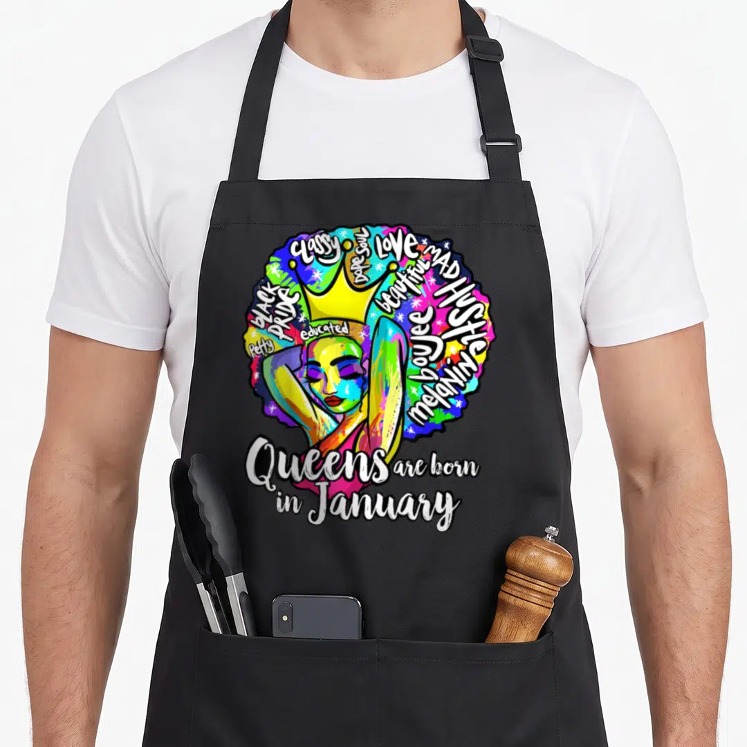 Capricorn queen apron - Colorful woman with crown and afro containing words like melanin and black pride above queens — shown on a black cotton canvas apron against a white background