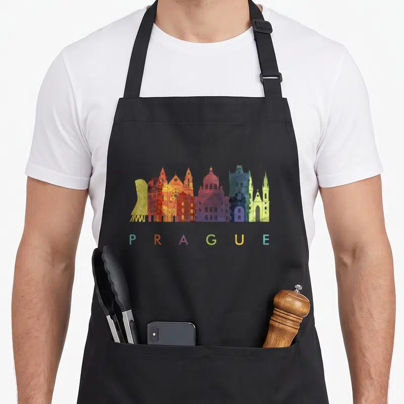 Travel family aprons - Colorful geometric Prague skyline with spaced lettering in yellow red orange purple blue green — shown on a black cotton canvas apron against a white background