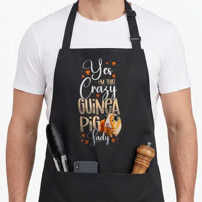 Cute comfort crazy guinea lady apron - Stacked Yes I'm That Crazy Guinea Pig Lady text with tricolor guinea pig — shown on a black cotton canvas apron against a white background