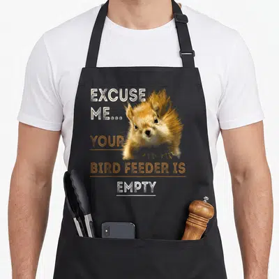 Bird squirrel aprons - Squirrel photo with text Excuse Me Your Bird Feeder Is Empty in orange and white — shown on a black cotton canvas apron against a white background