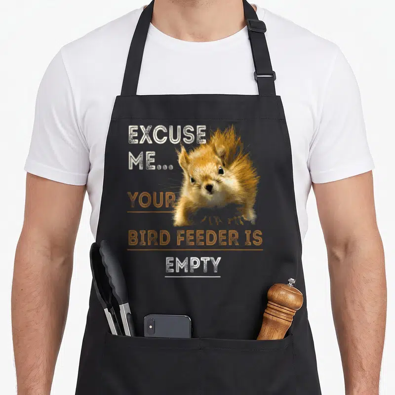 Bird squirrel aprons - Squirrel photo with text Excuse Me Your Bird Feeder Is Empty in orange and white — shown on a black cotton canvas apron against a white background