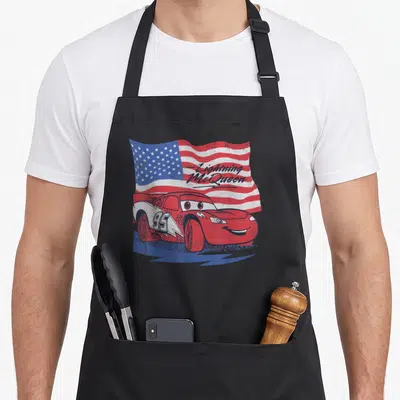 Funny flag car apron - Red race car 95 over waving US flag with Lightning McQueen script — shown on a black cotton canvas apron against a white background