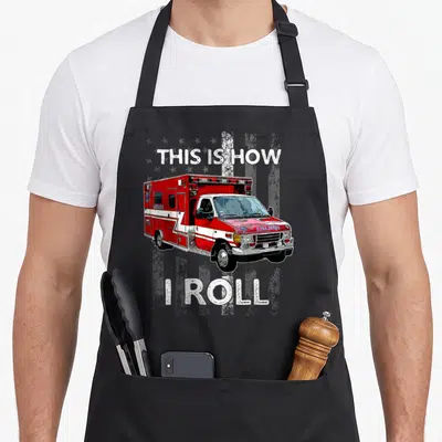 Roll ambulance girl apron - Red and white ambulance on distressed flag with text THIS IS HOW I ROLL — shown on a black cotton canvas apron against a white background