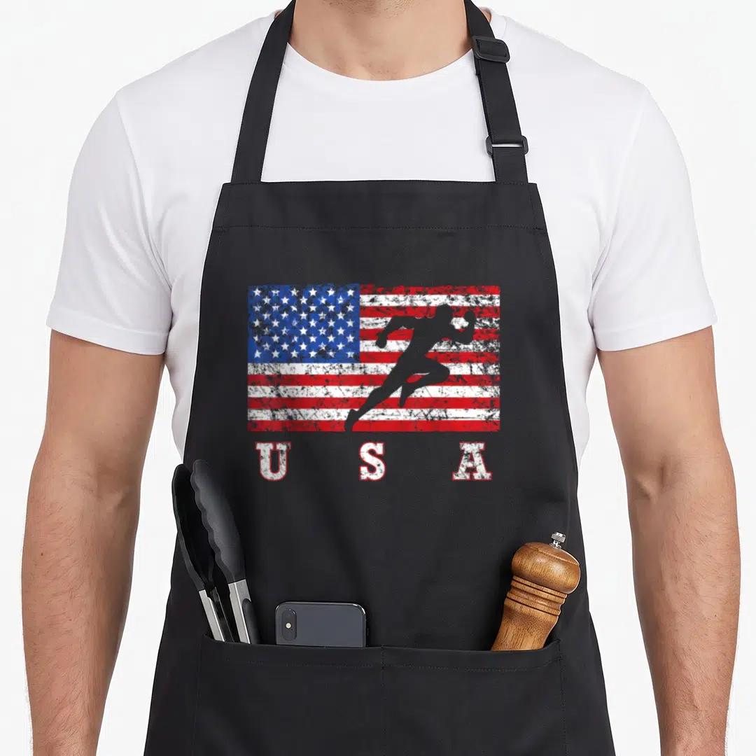 Track american flag apron - Distressed US flag with running silhouette and USA text below — shown on a black cotton canvas apron against a white background