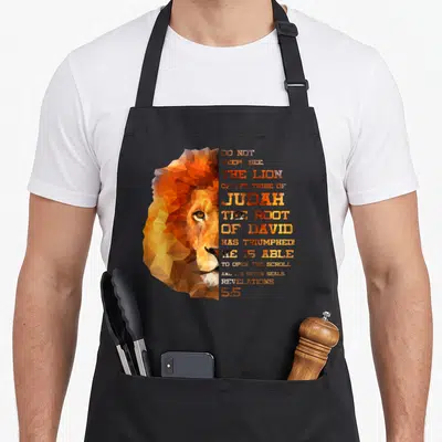Christ lions apron - Geometric lion head in orange and brown next to stacked Revelations 5:5 text — shown on a black cotton canvas apron against a white background