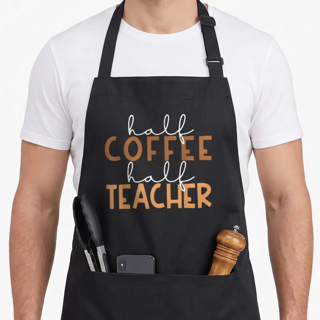 School teacher half apron - White script and tan block text reading half COFFEE half TEACHER stacked vertically — shown on a black cotton canvas apron against a white background