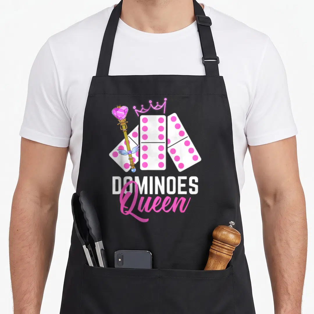 Dominoe domino queen apron - Three fanned dominoes with pink dots, a crown, scepter, and stacked DOMINOES Queen text — shown on a black cotton canvas apron against a white background