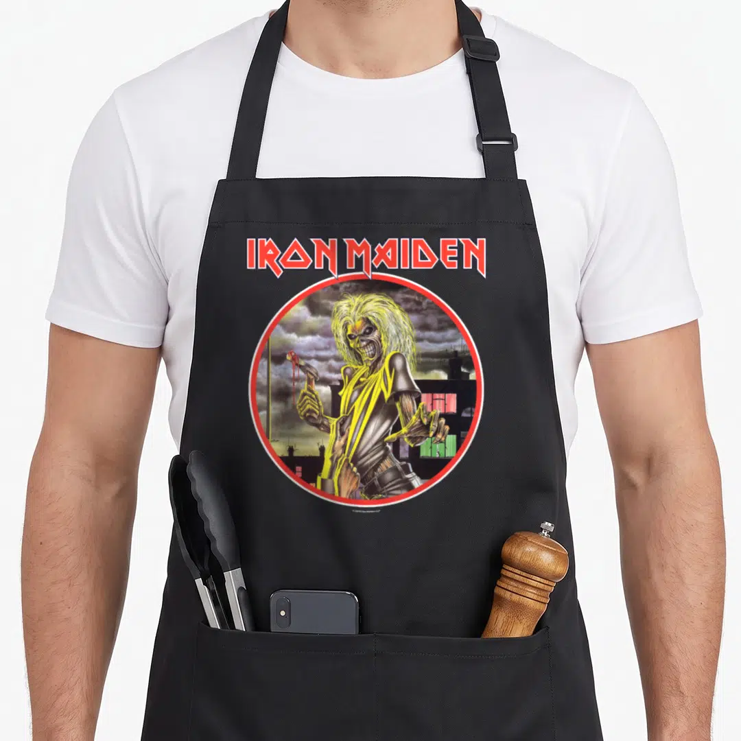 Funny camping apron - IRON MAIDEN text above Eddie standing in a circle with stormy skyline background — shown on a black cotton canvas apron against a white background