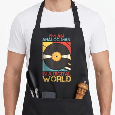 Analog vinyl apron - Vinyl record graphic with red yellow and blue sunburst and slogan text — shown on a black cotton canvas apron against a white background