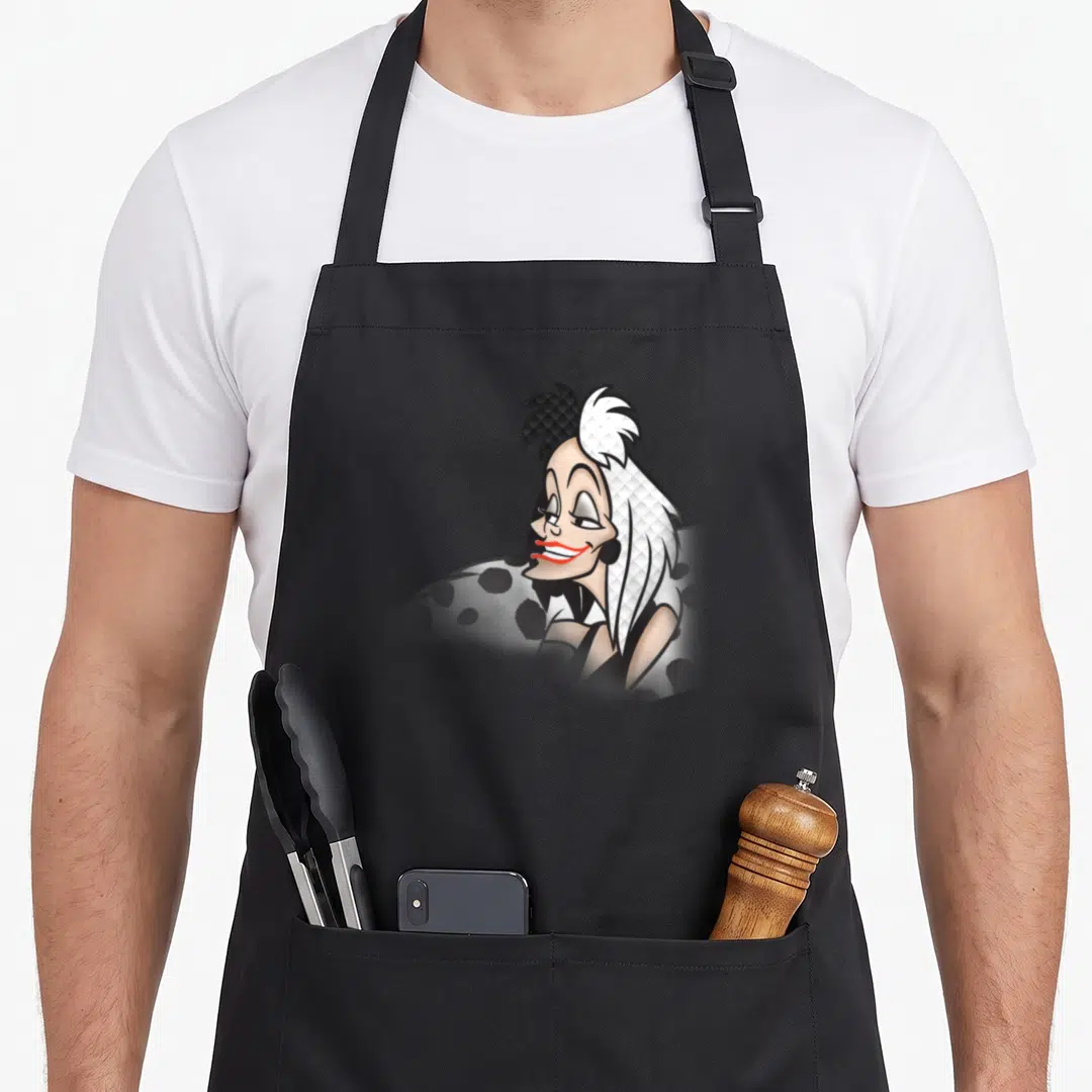 Evil cruller apron - Cartoon woman with split black and white hair and red lips on black background — shown on a black cotton canvas apron against a white background