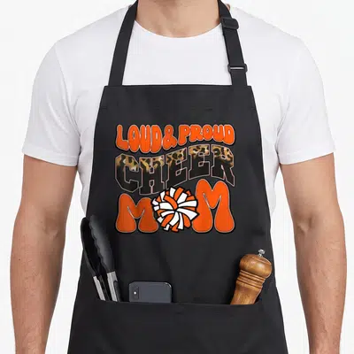 Proud crew aprons - Stacked LOUD PROUD CHEER MOM text with orange white pom-pom and leopard print CHEER letters — shown on a black cotton canvas apron against a white background