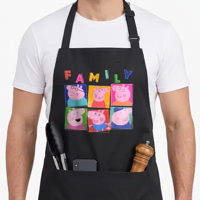 Box family aprons - Arched FAMILY text above six colored square portraits of a pig family in cartoon style — shown on a black cotton canvas apron against a white background