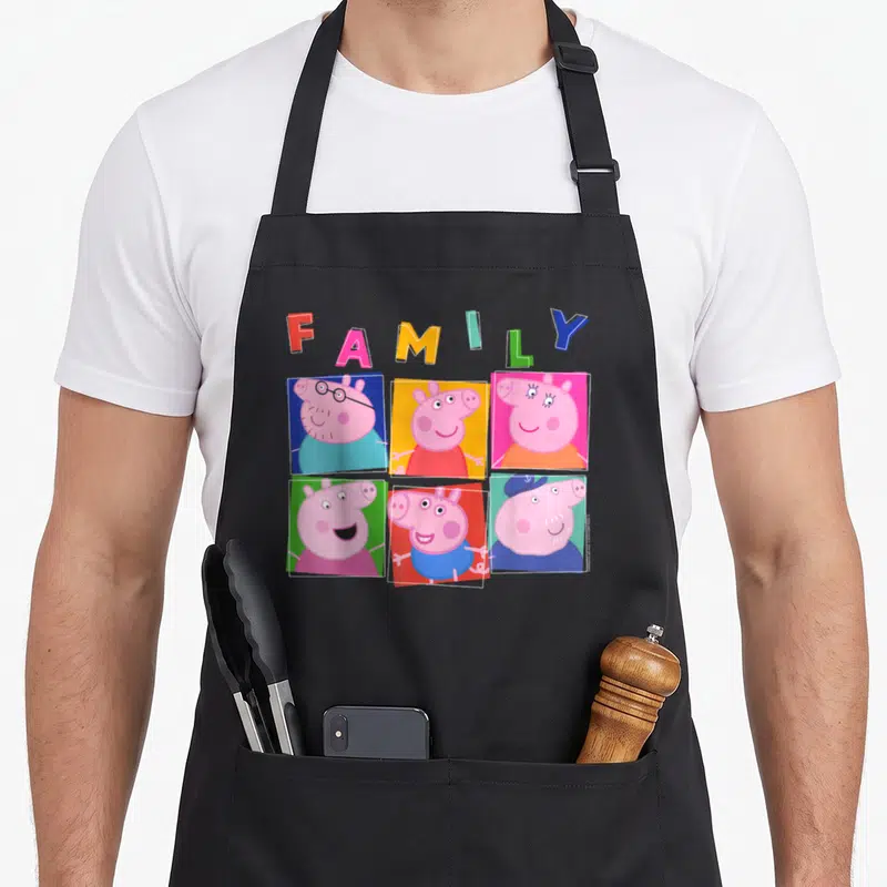 Box family aprons - Arched FAMILY text above six colored square portraits of a pig family in cartoon style — shown on a black cotton canvas apron against a white background